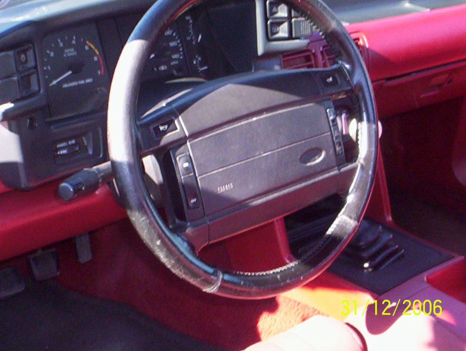 1990 Ford Mustang interior with red upholstery, black steering wheel, and dashboard gauges