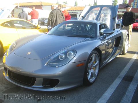 1985 Ford Mustang - A silver Porsche Carrera GT is displayed at a car show with its distinctive doors open.