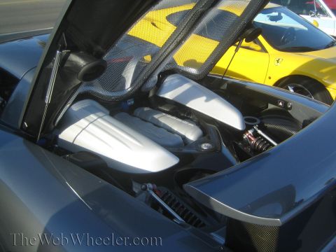 1985 Ford Mustang - The engine bay of a dark grey car is open, with a yellow Ferrari visible in the background.