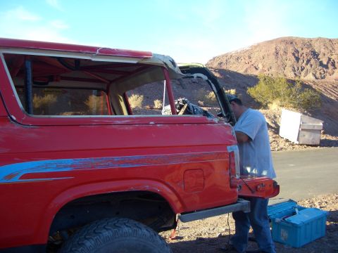 1985 Ford Bronco - A person is working on the rear of a red SUV, which appears to be undergoing some modifications or repairs.