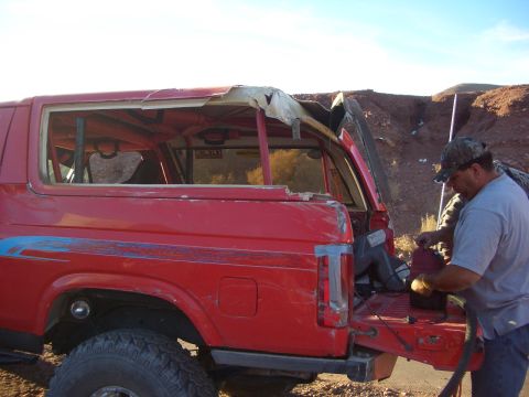 1985 Ford Bronco - A man works on the back of a red Ford Bronco with a damaged roof in an outdoor setting.