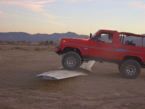1985 Ford Bronco - Red 1985 Ford Bronco navigates a ramp in a dry, open area with mountains in the background.