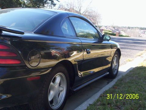 1995 Ford Mustang - Black 1995 Ford Mustang coupe parked on a street with houses in the background.