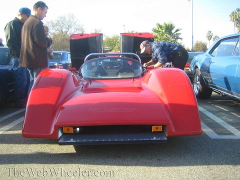 1985 Ford Mustang - A red sports car is displayed at an outdoor car show with other vehicles present.
