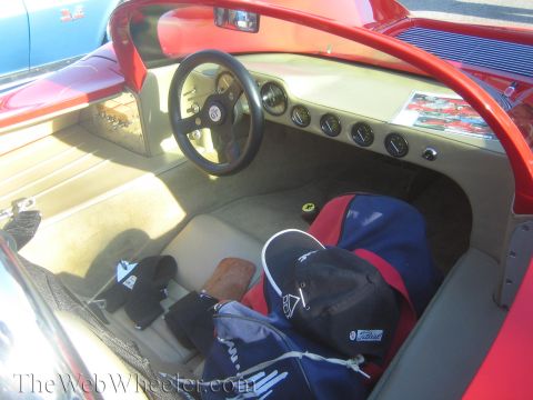 1985 Ford Mustang - Interior view of a red sports car, packed with bags and hats, at a car show.