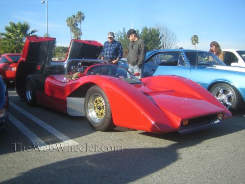1985 Ford Mustang - A red sports car with its doors open is displayed at an outdoor car show.