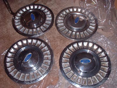 1997 Ford Crown Victoria - Four chrome Ford hubcaps with blue oval emblems are shown, likely for a Crown Victoria, though the specific year is not evident from the im…