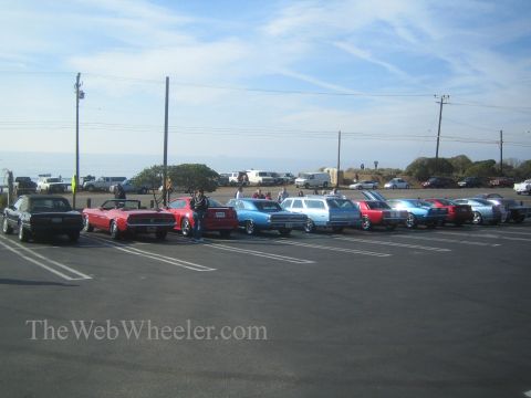 1985 Ford Mustang - A collection of vintage vehicles are parked in a lot overlooking the ocean on a sunny day.
