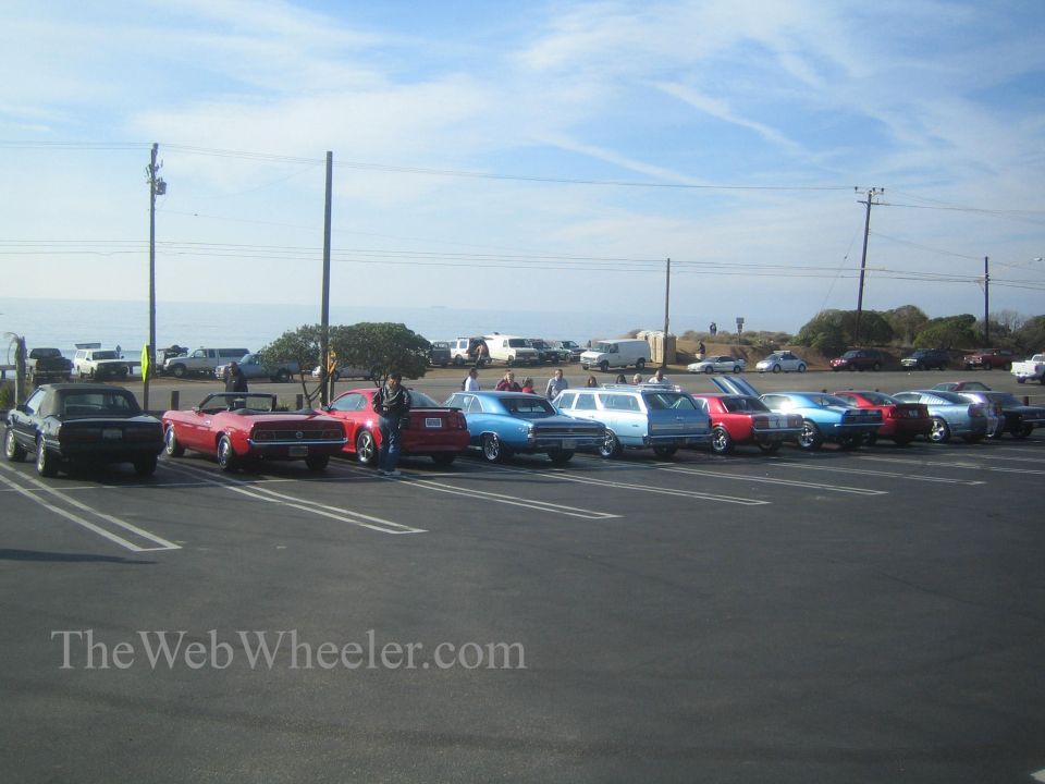 Cars parked by the ocean, including a red convertible and a blue station wagon