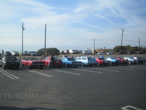 1985 Ford Mustang - A line of classic cars, including a red 1985 Ford Mustang convertible, are parked at an outdoor car show.