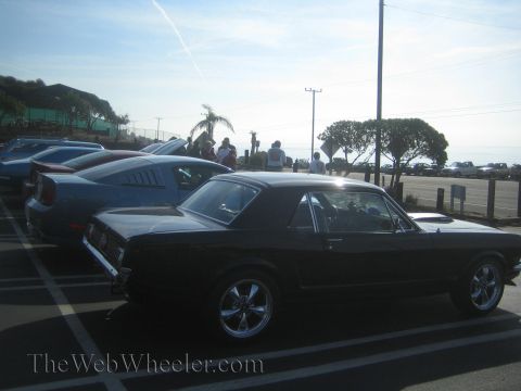 1985 Ford Mustang - A classic black Ford Mustang is parked in a lot with other vehicles under a bright sky.