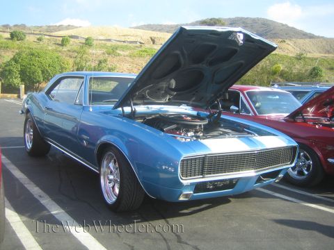 1985 Ford Mustang - A blue classic car with its hood open is parked next to a red car under a bright sky.