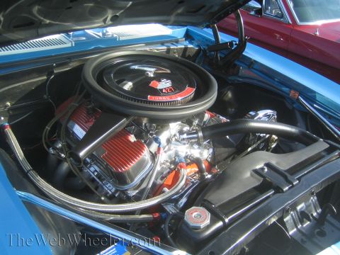 1985 Ford Mustang - Engine bay of a blue car with a 427 Turbo Jet engine, seen at a car show with another vehicle behind it.