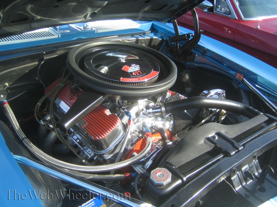 Blue car engine bay with chrome details and a black air cleaner with a red 427 Turbo Jet emblem. A red car is visible in the background