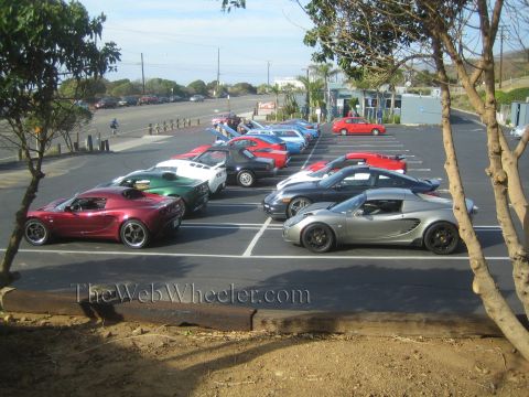 1985 Ford Mustang - Multiple sports cars are gathered in a parking lot on a sunny day.