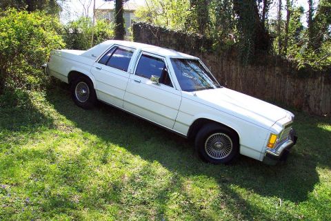 1985 Ford Crown Victoria LTD - White 1985 Ford Crown Victoria LTD parked on a grassy slope next to a wooden fence.