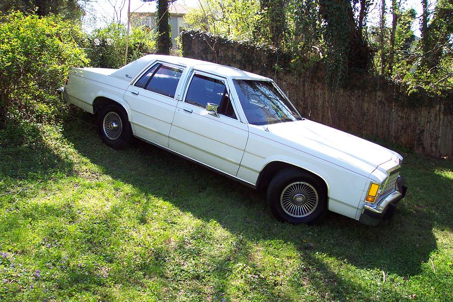 White 1985 Ford Crown Victoria LTD parked on a grassy slope next to a wooden fence