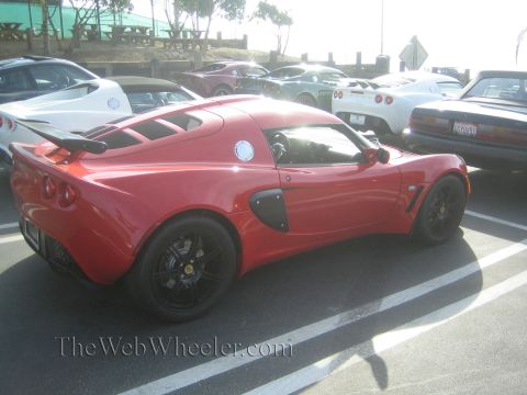 1985 Ford Mustang - A red Lotus Elise is parked at a car show, alongside other vehicles.