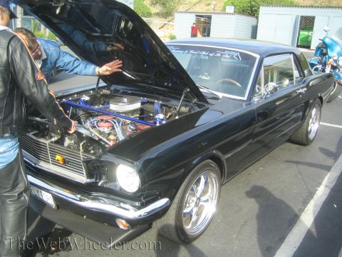 1985 Ford Mustang - A black coupe with its hood open is examined by two individuals at a car show.