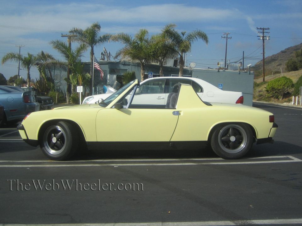 Yellow Porsche 914 Targa parked, side view. White sedan behind it