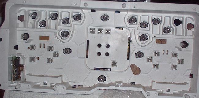 Back of a white plastic instrument cluster with numerous screw mounts and electrical connectors