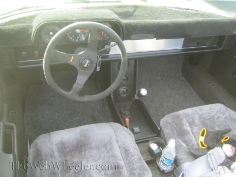 1985 Ford Mustang - The interior of a car shows fuzzy seat covers and a prominent steering wheel.