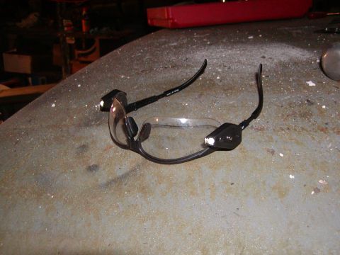 1991 Ford Bronco - Safety glasses with built-in lights rest on a dusty surface in a workshop.