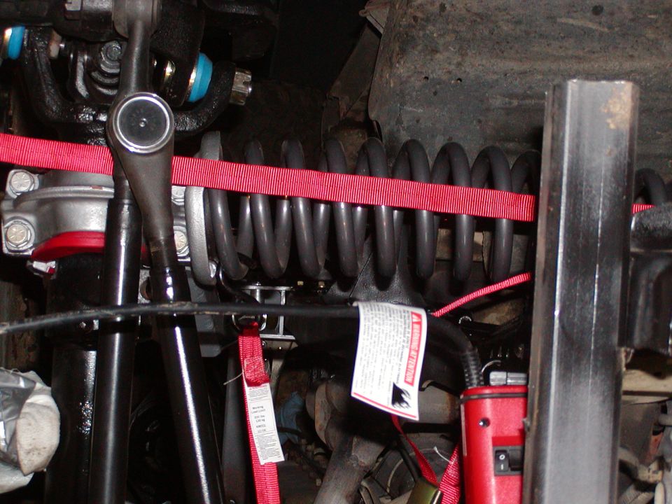 close-up of vehicle suspension with red straps around coil spring