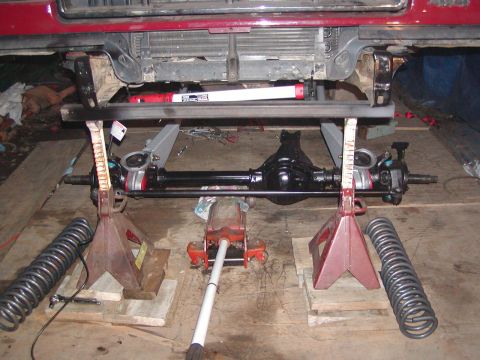 1991 Ford Bronco - Front axle assembly being worked on, supported by jack stands in a garage setting.