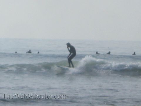 1985 Ford Mustang - A surfer catches a wave while others wait in the ocean.
