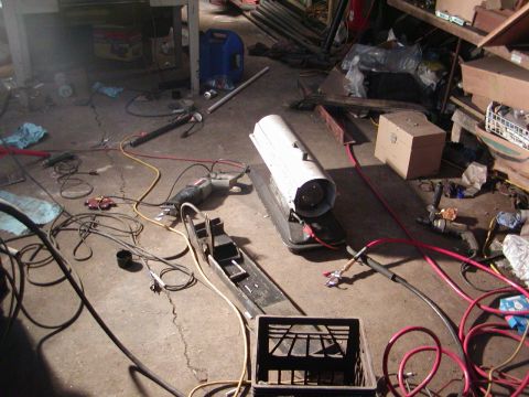 1991 Ford Bronco - A cluttered garage scene shows a portable heater, power tools, and various electrical cords scattered across the concrete floor.
