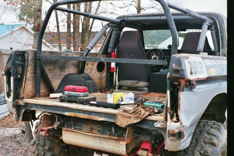 1978 Ford Bronco - The interior and bed of a heavily modified off-road vehicle are shown, a roll cage and various tools.