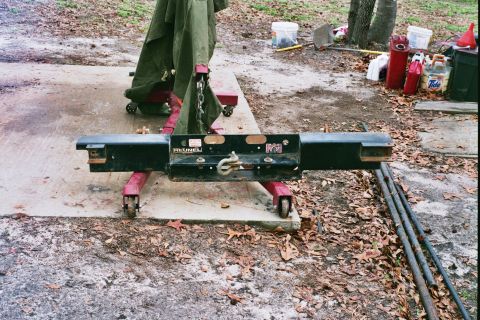 1978 Ford Bronco - A black tow hitch is supported by a red engine hoist on a concrete pad outdoors.