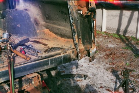 1978 Ford Bronco - The rear section of a vehicle shows extensive rust and damage, with tools scattered on the surface.