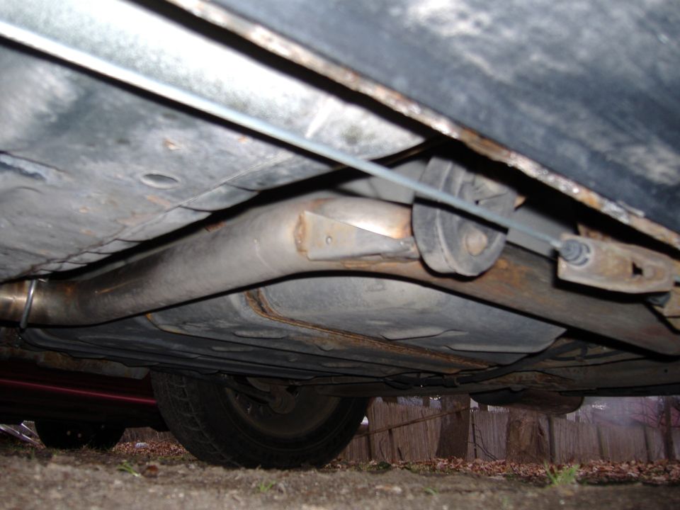 Underside view of a car's exhaust system and undercarriage, showing rust and wear
