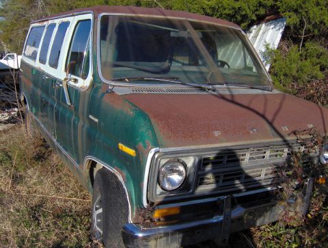 1978 Ford Bronco - This heavily rusted van, likely a Ford Econoline, sits abandoned amidst overgrown vegetation.