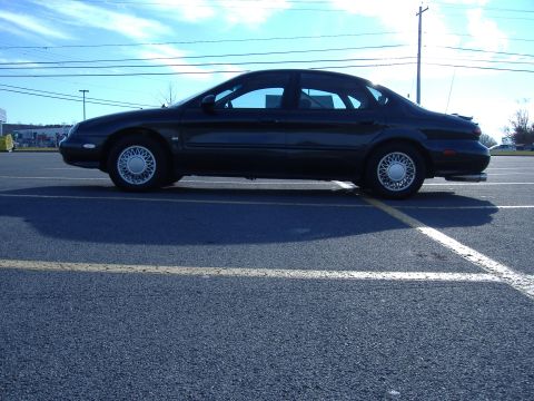 1998 Ford Taurus - Side profile of a 1998 Ford Taurus sedan parked in an asphalt lot under a blue sky.