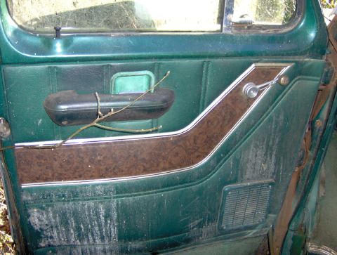 1978 Ford Bronco - Interior door panel detail green upholstery, wood grain trim, and a chrome window crank.