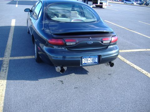 1998 Ford Taurus - The rear of a dark sedan is parked in a lot, showing its taillights, spoiler, and dual exhaust.