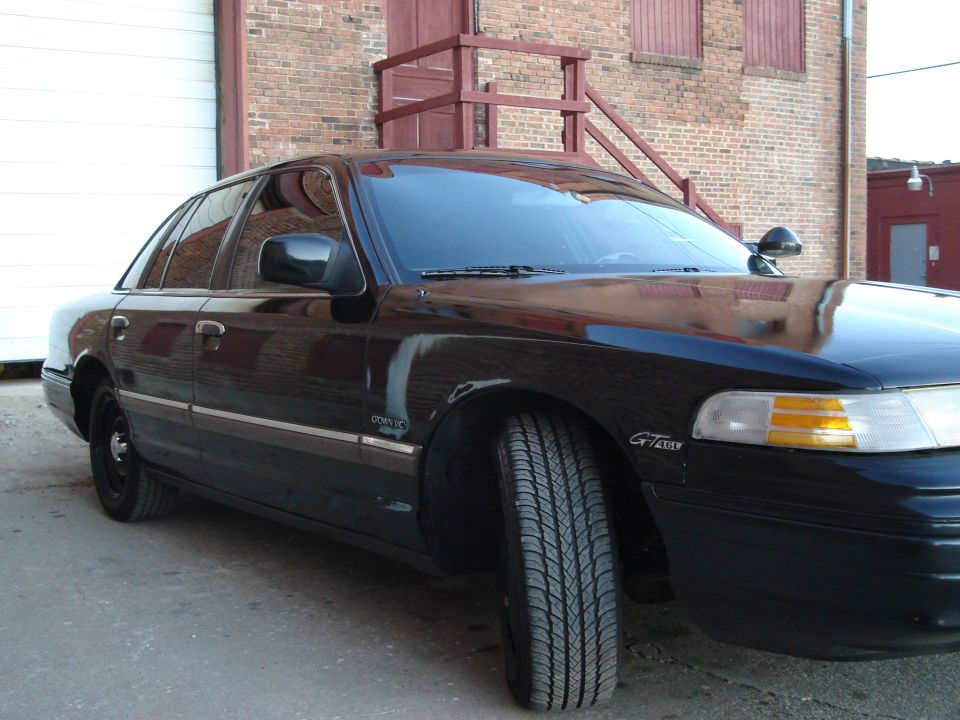 Black 1992 Ford Crown Victoria sedan, front 3/4 view, parked outside a brick building