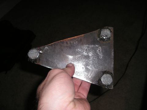 1996 Ford Bronco - A metal bracket with three bolts is held by a hand against a dark background.
