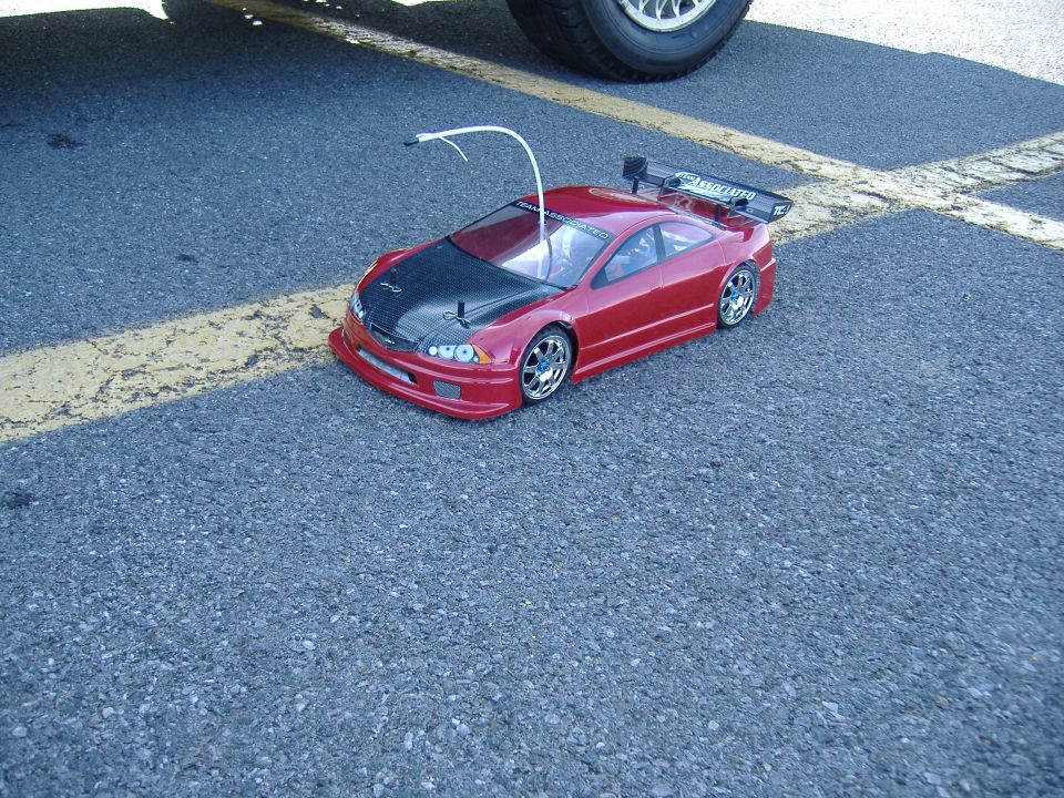 Metallic red RC touring car with carbon-look hood and rear wing on asphalt