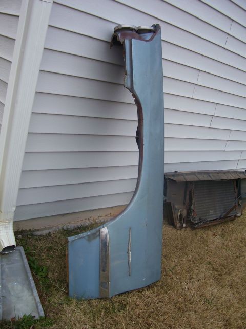 1965 Pontiac Catalina - A detached car fender and a radiator sit on the grass beside a house.