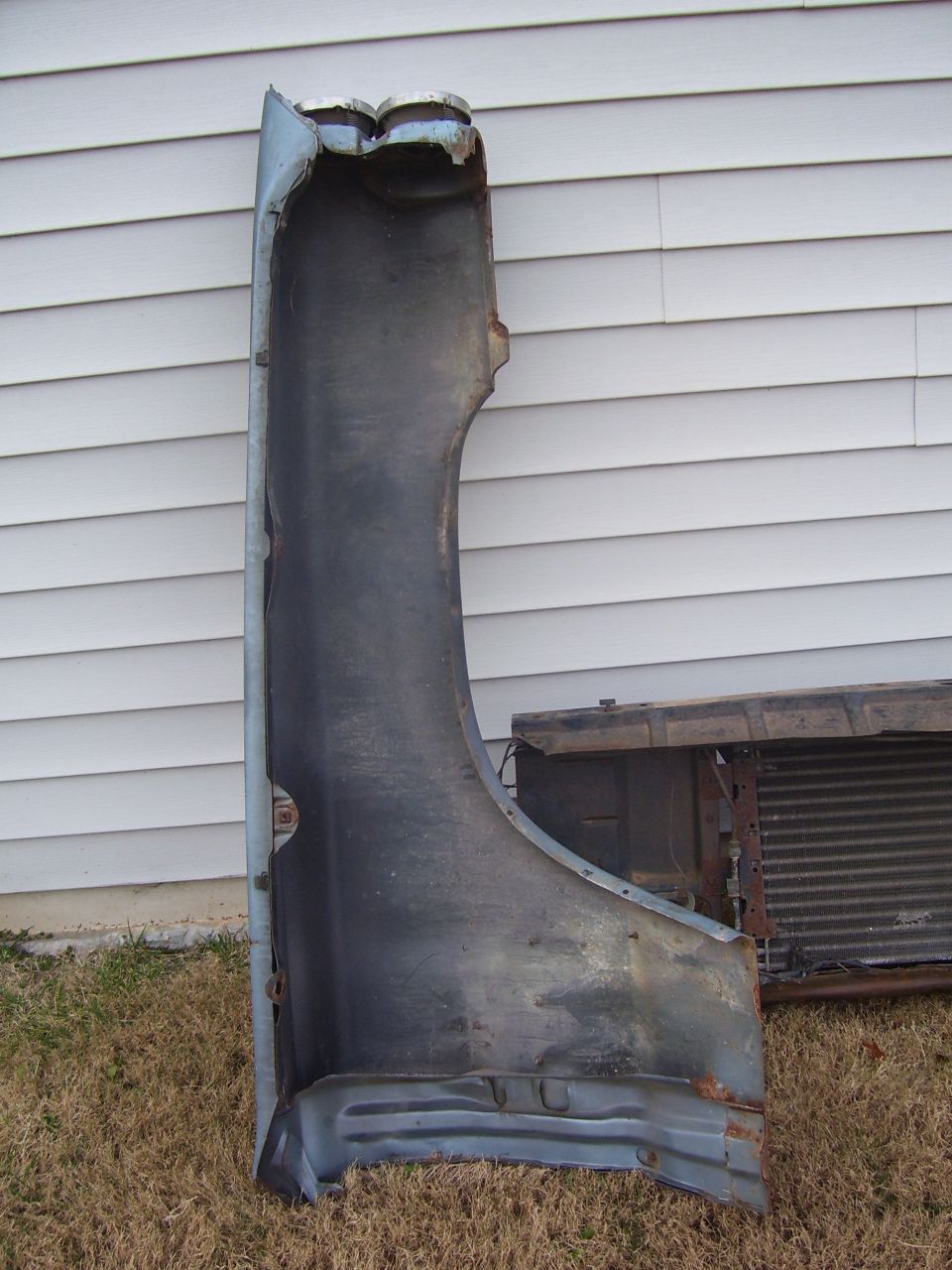 car fender and radiator sitting on grass in front of a house