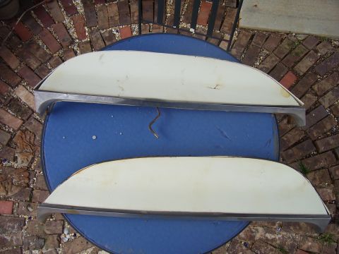 1965 Pontiac Catalina - Two car trim pieces are displayed on a blue table, with a brick patio in the background.