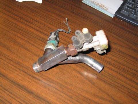 1991 Ford Crown Victoria LTD - A close-up view of a vacuum hose and sensor assembly, likely a car part, resting on a wooden desk.