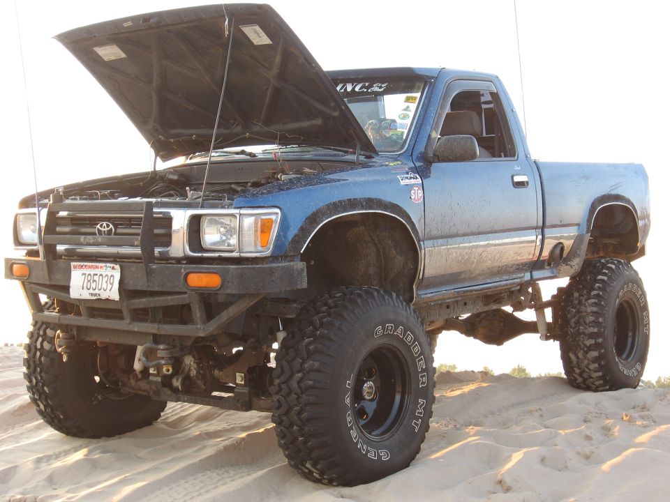 Blue lifted Toyota pickup truck, hood open, parked on sand. License plate reads 785039