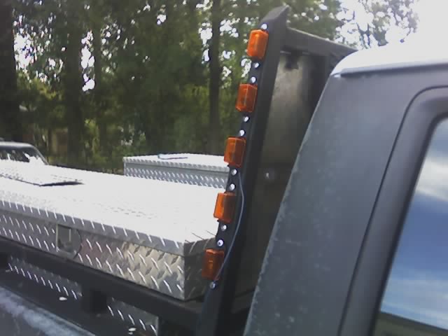 Black headache rack with vertical row of amber marker lights and diamond-plate toolbox on a truck bed