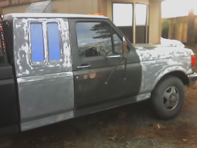 Ford F-Series truck with primer spots, dual rear wheels, and custom rear windows