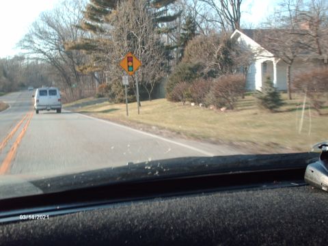 1995 Ford Probe - A white van drives down a two-lane road past a traffic signal sign and a small house.